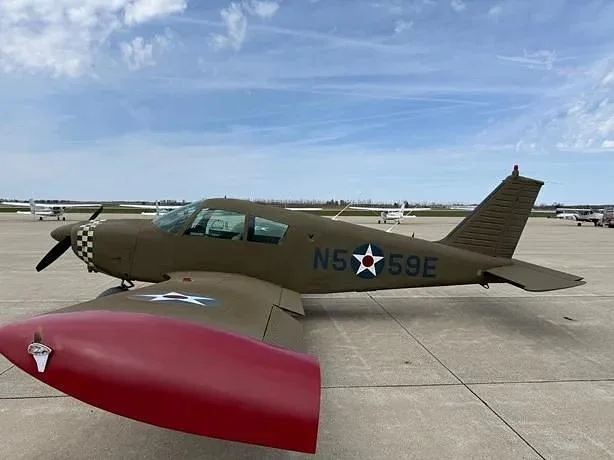 A side view of a green Grumman AA-5 Traveler aircraft with a red wingtip and US star insignia, showing the tail number N559E, on an airfield.