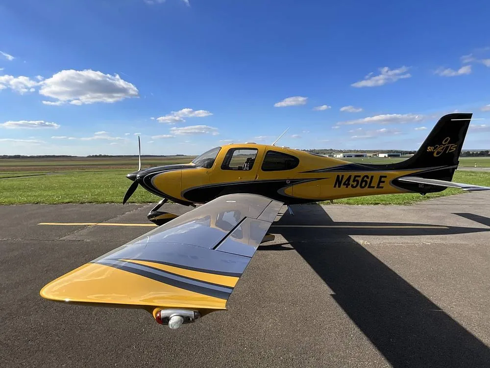 A yellow and black Cirrus SR22 aircraft with registration N456LE parked on an airfield, showing the wing and tail.