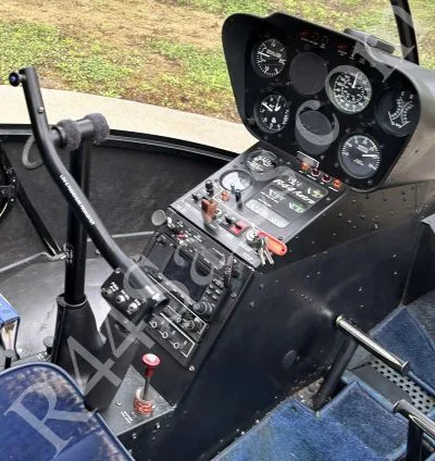 The cockpit of a Robinson R44 helicopter, showing the instrument panel and cyclic control.
