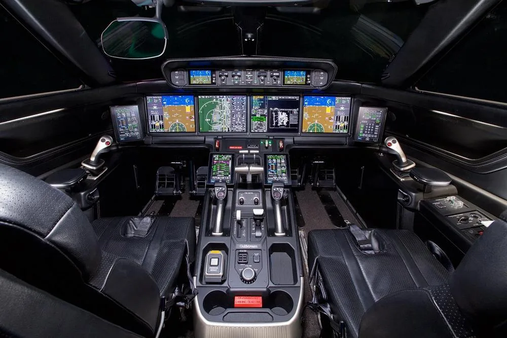 The modern cockpit of a Gulfstream G600/G650 business jet with multiple large digital displays and side-stick controls.
