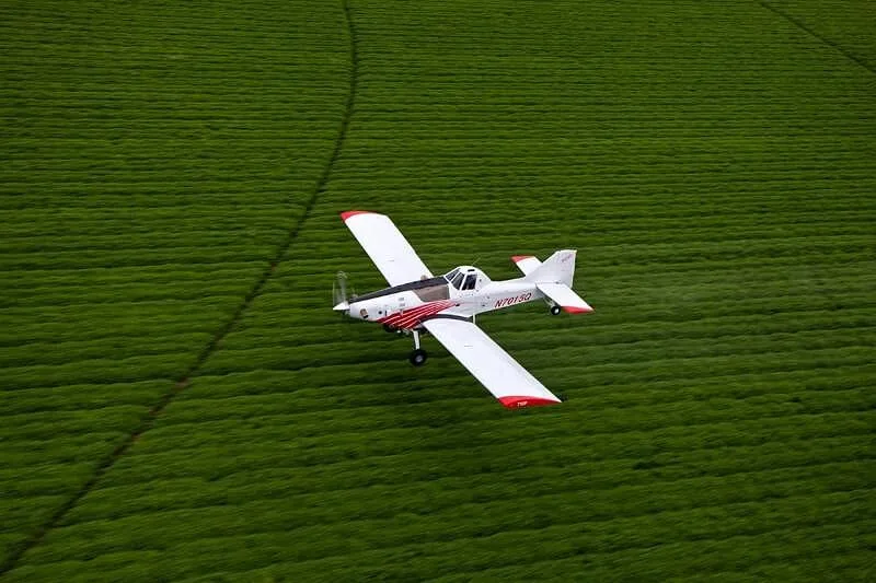 An aerial view of a white and red agricultural aircraft flying low over a green field.
