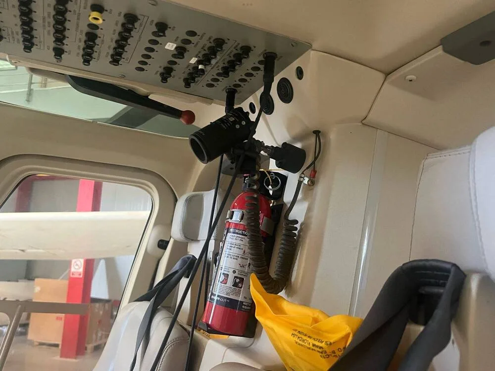 An overhead panel, a mounted fire extinguisher, and a yellow safety bag in the helicopter's cockpit area.