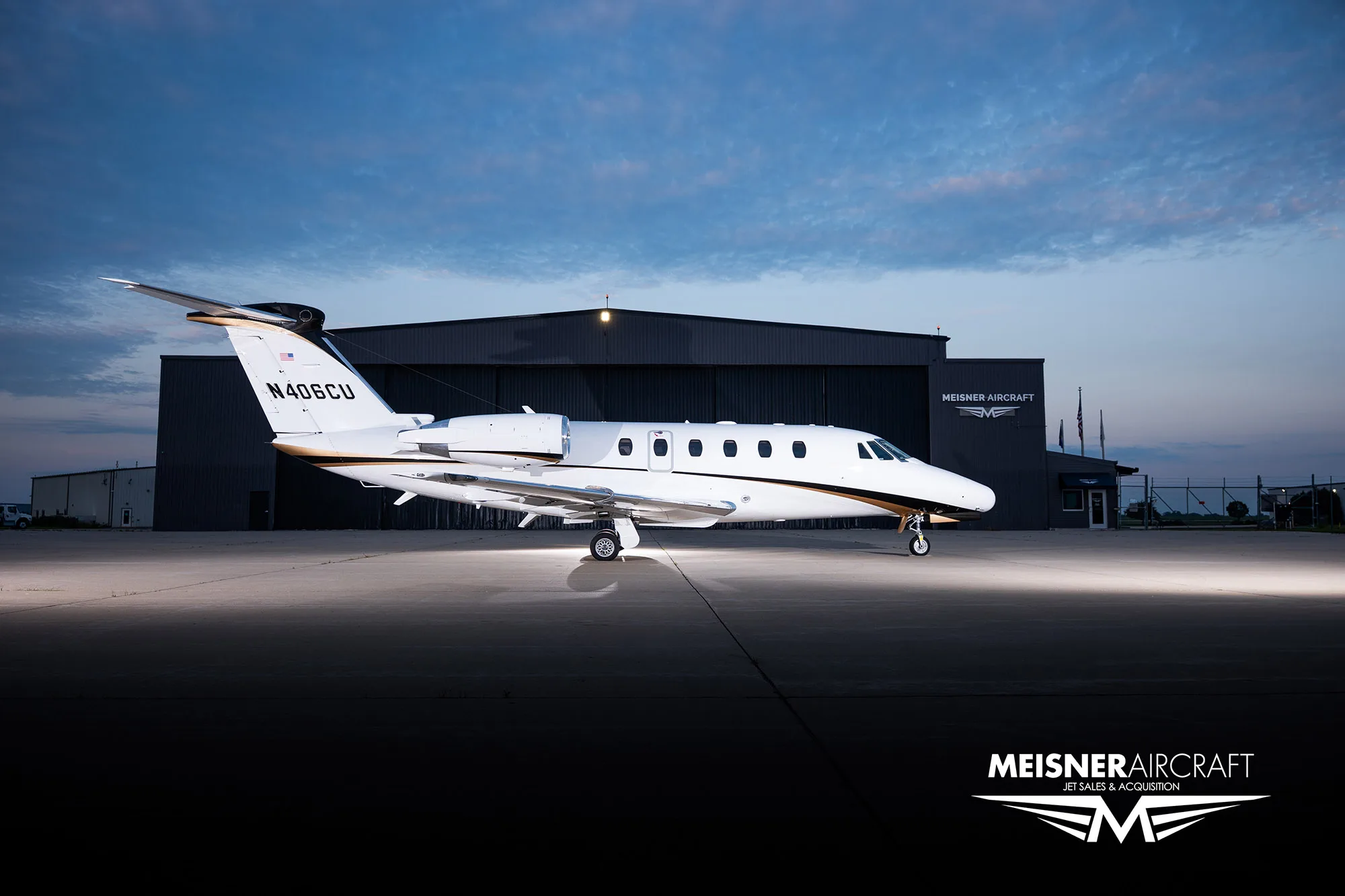 A white and black Cessna Citation business jet (N406CU) parked in front of a hangar at dusk.