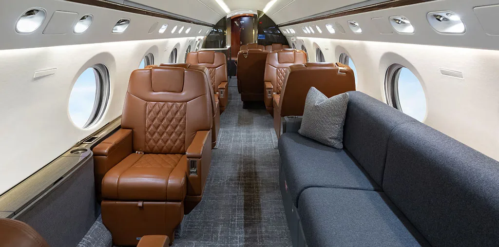 The luxurious cabin interior of a business jet, featuring brown leather seats and a grey sofa.