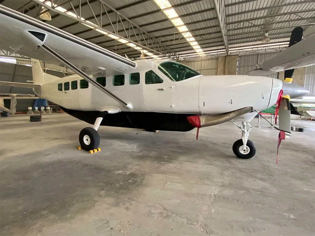 A white Cessna Caravan aircraft with a black underbelly is parked inside a large hangar.