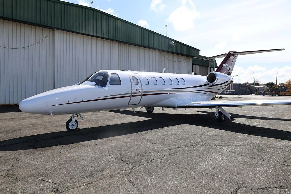 A white private jet with red and black accents, tail number N509WC, parked on an tarmac with a hangar in the background.