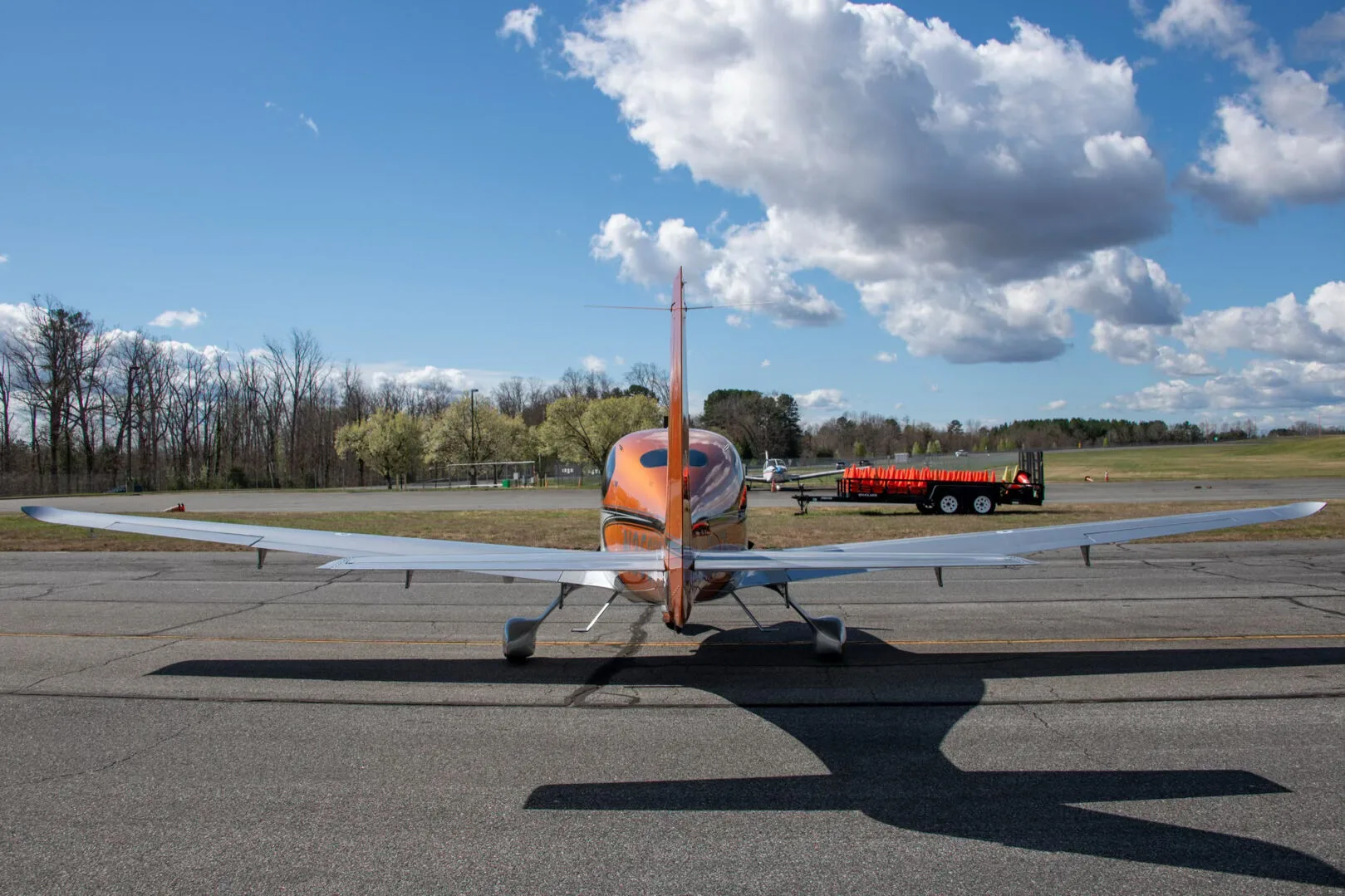 A rear view of a metallic orange and silver Cirrus SR22 aircraft (N356HT) parked on an asphalt ramp.