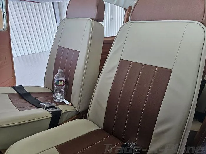 Two light beige and brown aircraft seats with a water bottle on one seat inside a cabin.