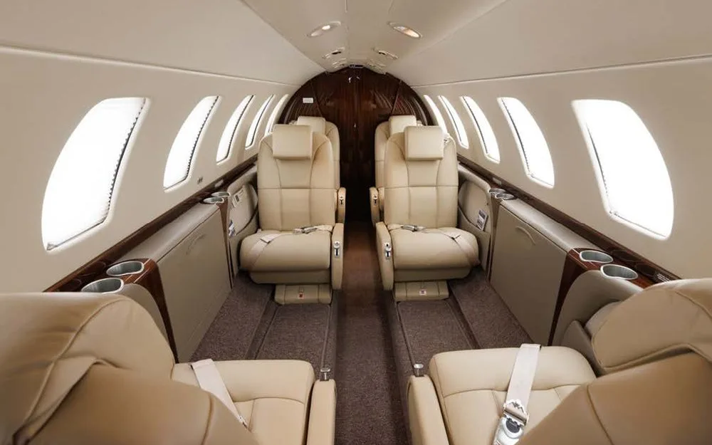 The interior cabin of a private jet with light tan leather seats facing each other.