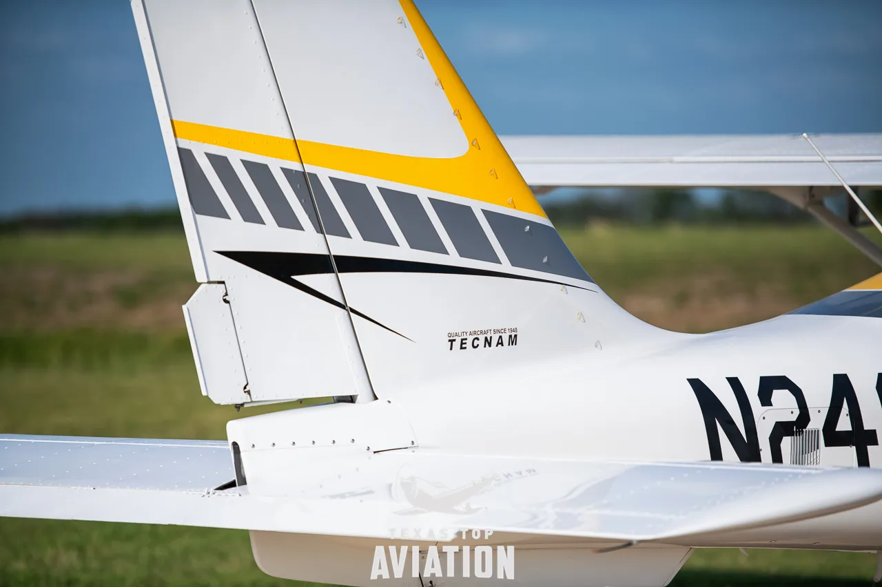 A close-up of the white and yellow tail of a Tecnam aircraft, showing the 'Tecnam' logo and part of the registration.