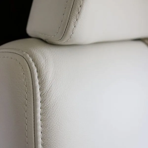 A close-up view of the white leather upholstery and stitching on an aircraft seat.