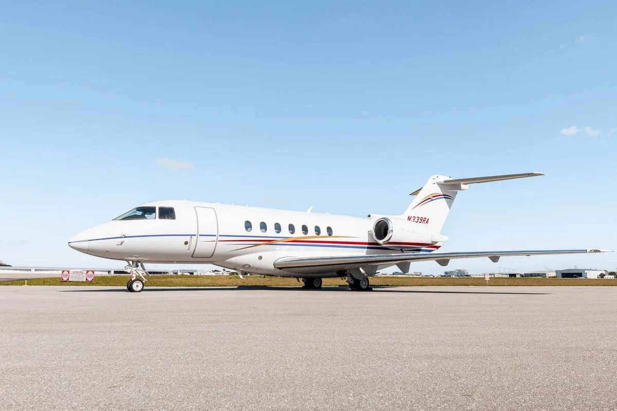 A white Hawker 800XP business jet with red and blue stripes, registration N339RA, parked on the tarmac under a clear sky.