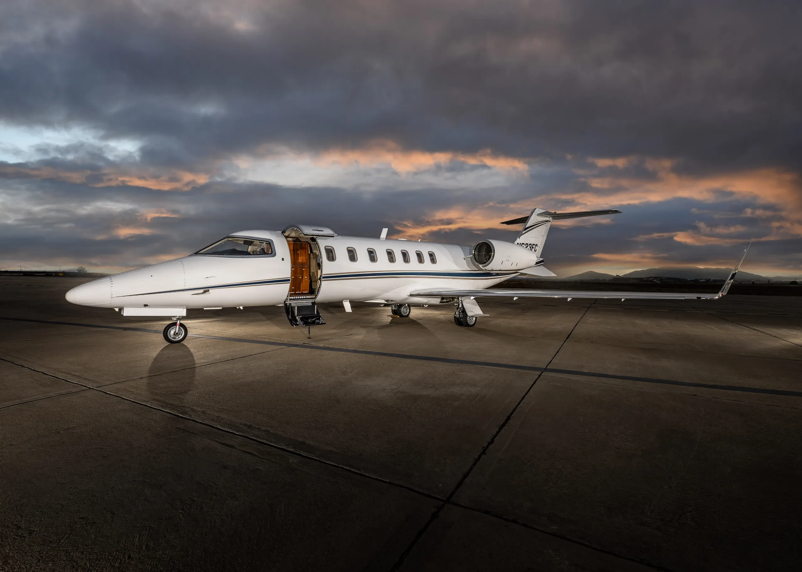 A white Learjet 60 with its main cabin door open, registration N623FC, parked on an airfield at sunset.
