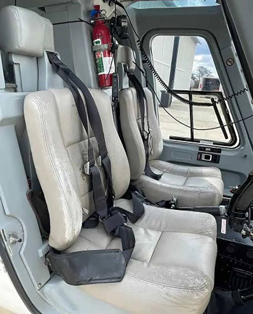 The two front seats of a helicopter cabin, with a fire extinguisher mounted nearby.
