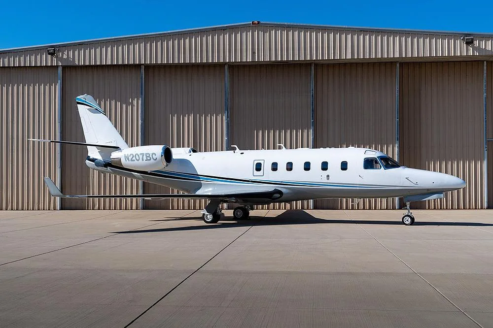 A white and blue Cessna Citation CJ3 (N207BC) business jet parked on a tarmac in front of a hangar.