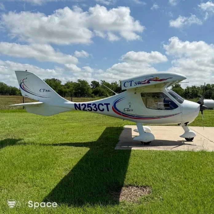 A white Flight Design CT Light Sport aircraft, N253CT, is parked on a concrete pad with grass and trees in the background.