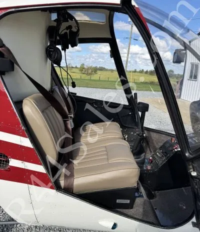 The tan leather seats and interior of a Robinson R22 helicopter viewed from the open door.
