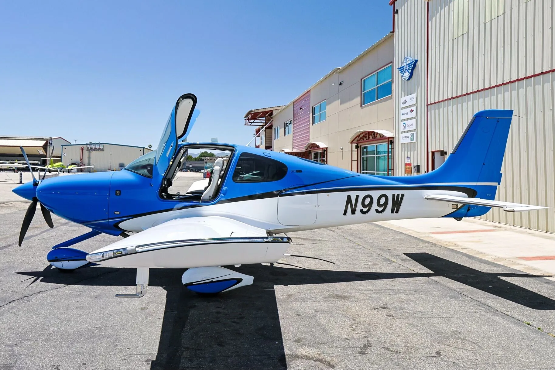 A blue and white Cirrus SR22 aircraft (N99W) with open doors, parked on an airfield.