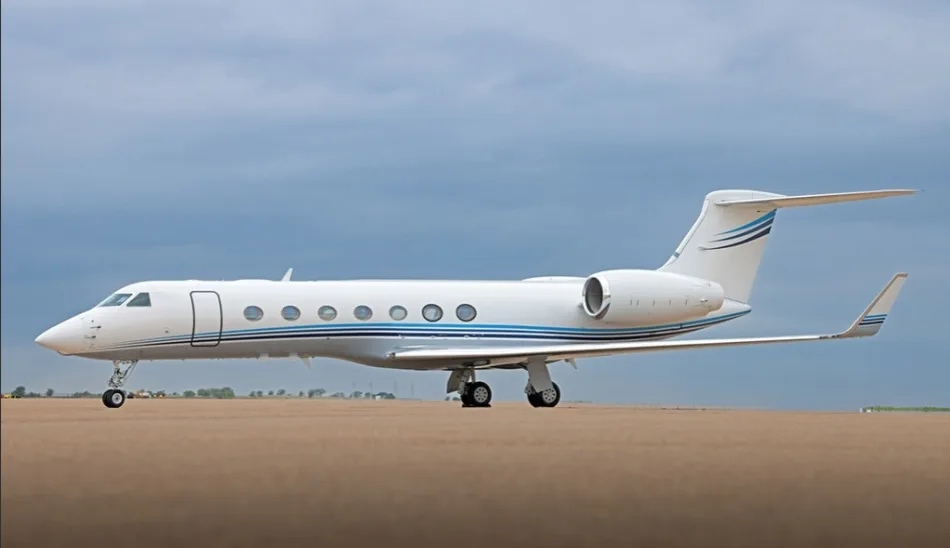 A white Gulfstream G650 business jet with blue accent stripes parked on an airfield under a cloudy sky.