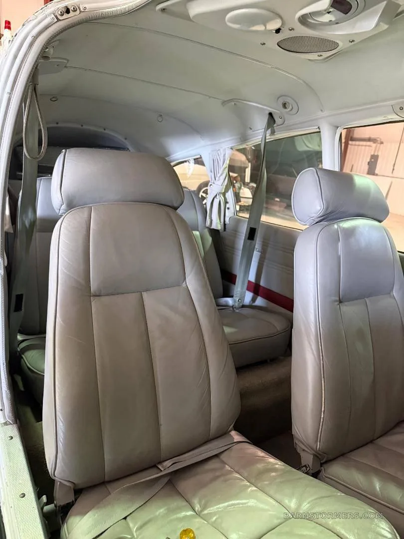 The light gray leather interior of a small aircraft cabin, showing two front seats and a glimpse of the rear seats.