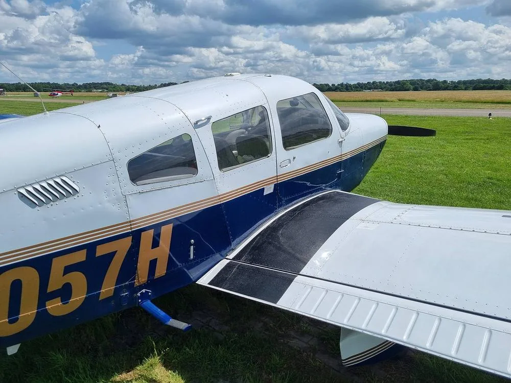 A close-up view of the fuselage and wing of the Piper PA-28 Cherokee, registration N6057H, showing its blue and white paint scheme.