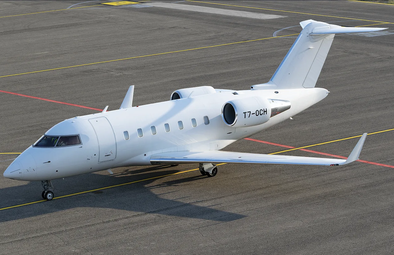 An all-white Bombardier Challenger business jet with registration T7-0CH is parked on an airport tarmac.