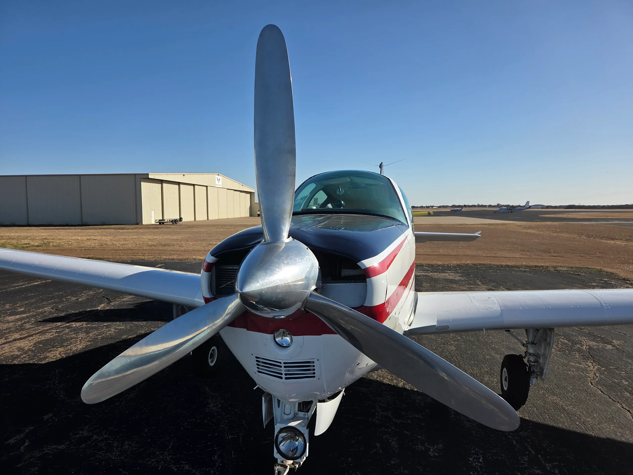A close-up front view of a white and red single-engine aircraft with a large propeller, parked on an asphalt ramp.