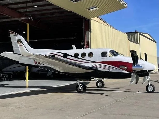 A white and red Beechcraft King Air 350i aircraft, registration N448CR, parked outside a hangar.