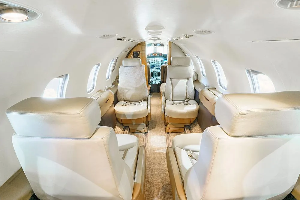 A wide-angle view of the aircraft cabin looking towards the cockpit, featuring light-colored leather seats and overhead lighting.