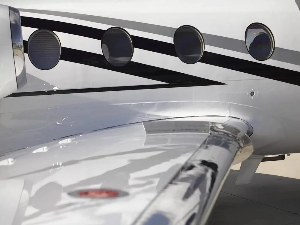 A close-up view of the white fuselage with black and grey stripes and the wing of the Cessna Citation M2, N440LN.