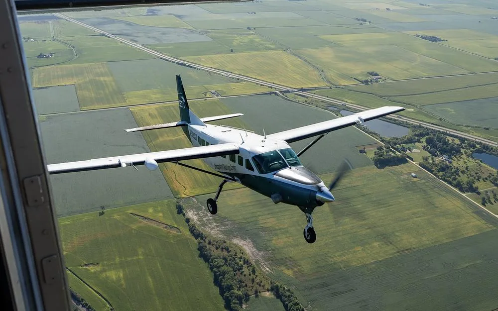 A teal and white single-engine turboprop aircraft, N901ST, flies over green agricultural fields.