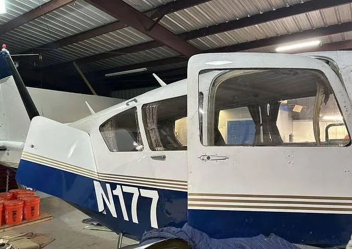 The rear fuselage of a white and blue N177 aircraft with an open door is seen inside a hangar.