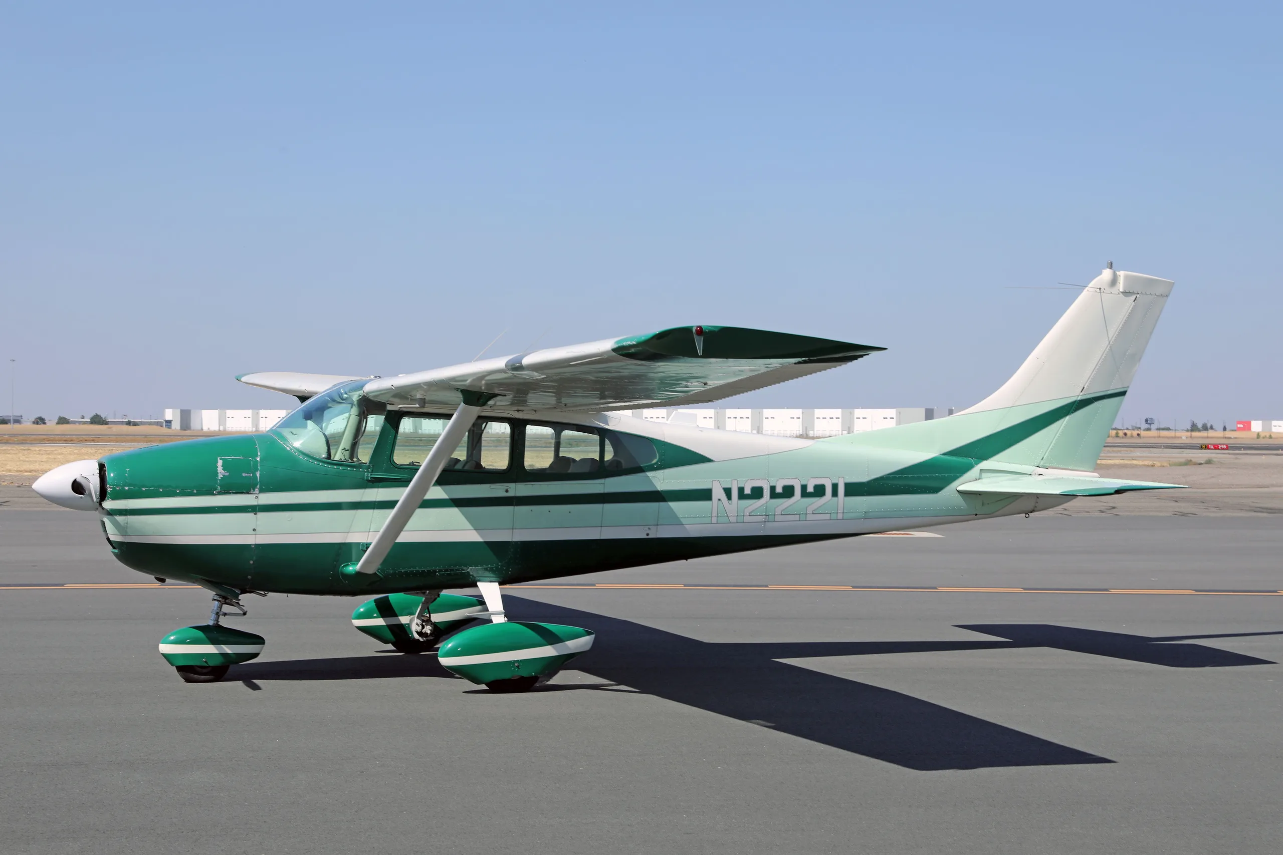 A green and white Cessna 182 Skylane N2221 parked on an airfield tarmac under a clear sky.