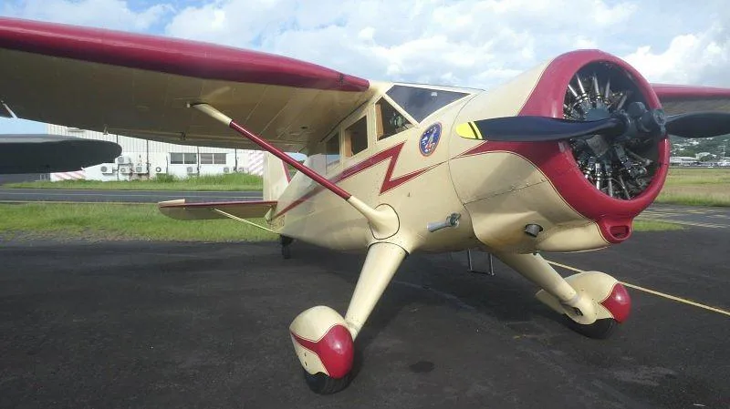 A vintage cream and red single-engine aircraft with a radial engine and fixed landing gear, parked on an asphalt tarmac.