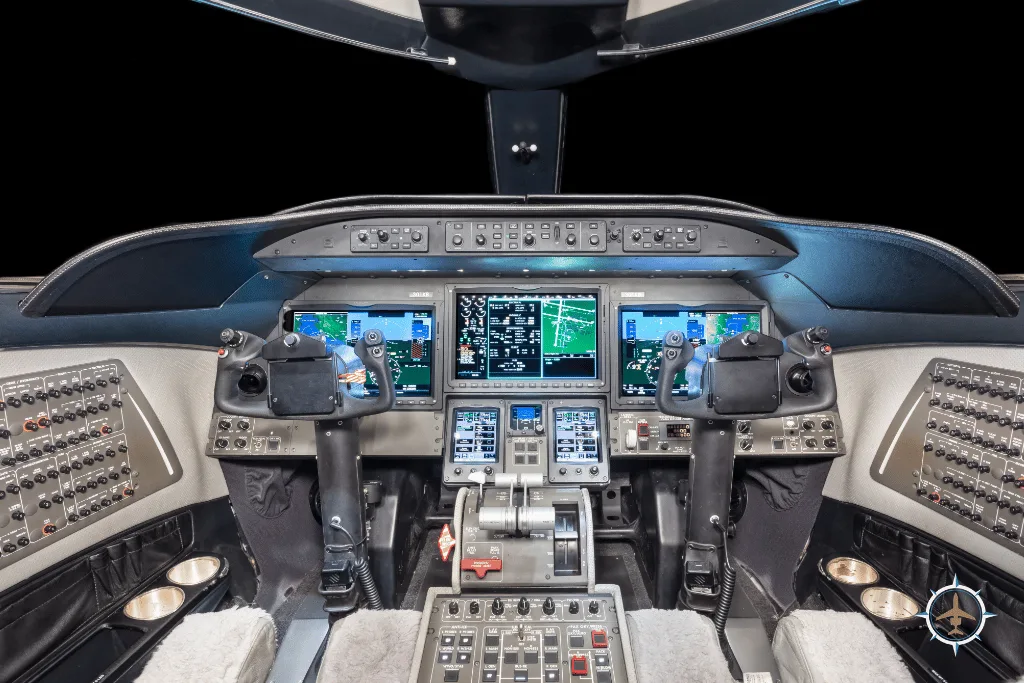 The modern cockpit of a business jet with multiple display screens and control yokes.