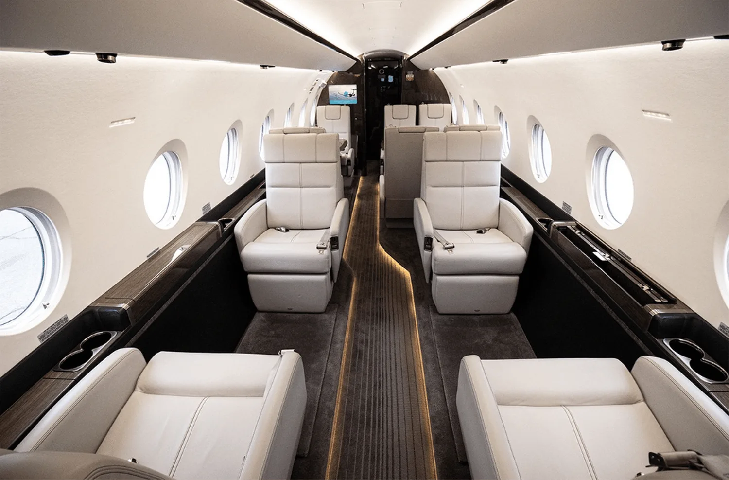 The spacious interior cabin of a private jet with light-colored leather seats, large windows, and overhead lighting.