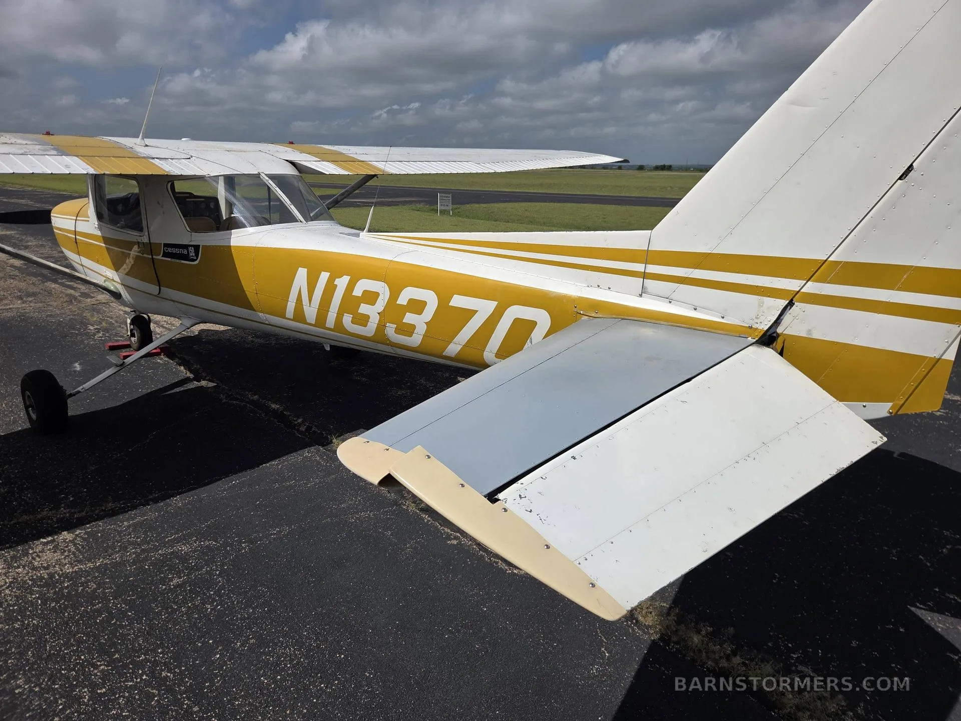A close-up view of the white and yellow tail section and right wing of a light aircraft (N13370) on an asphalt ramp.