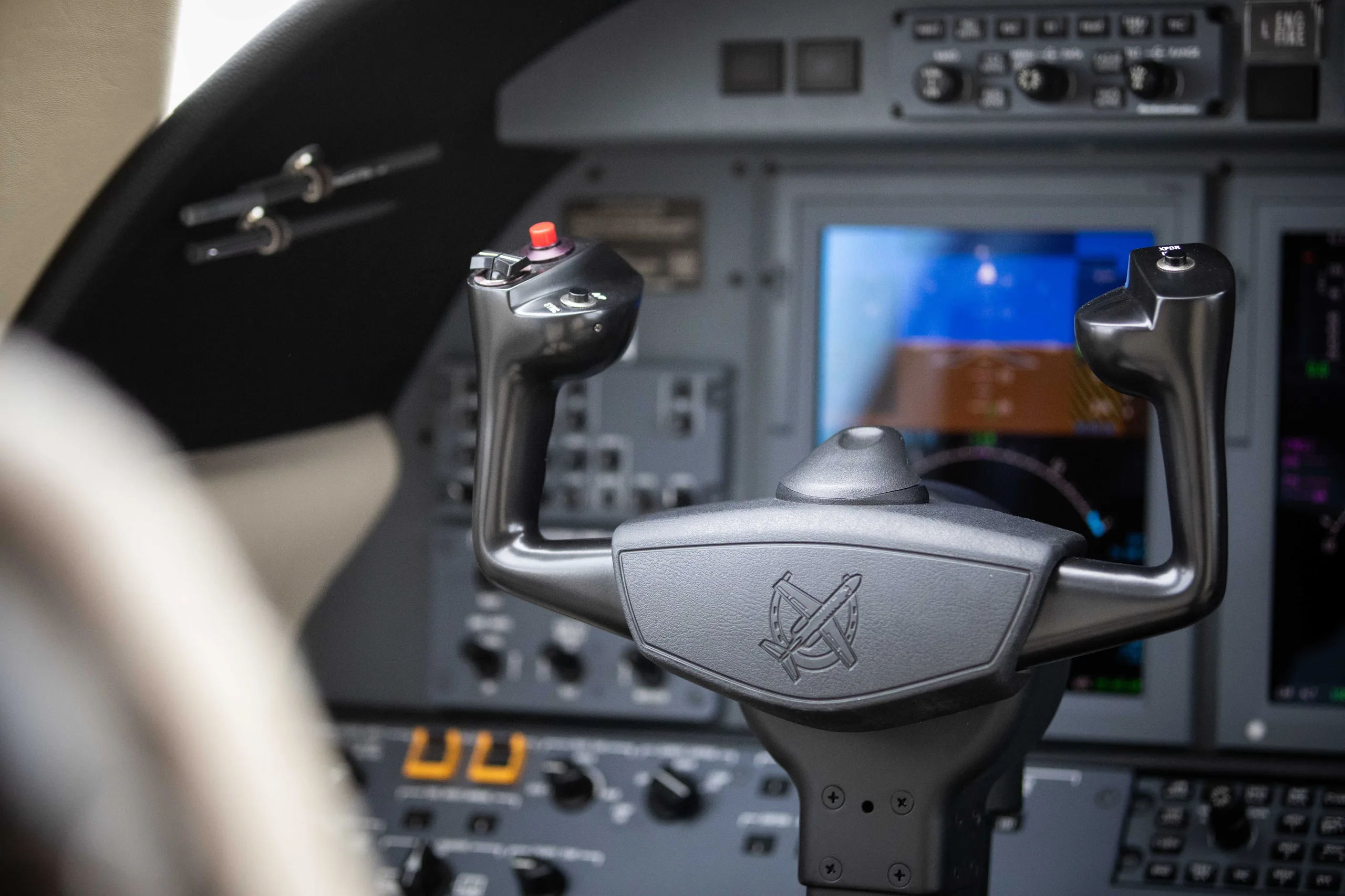 A close-up of an aircraft's control yoke with a red button and digital screens in the background.