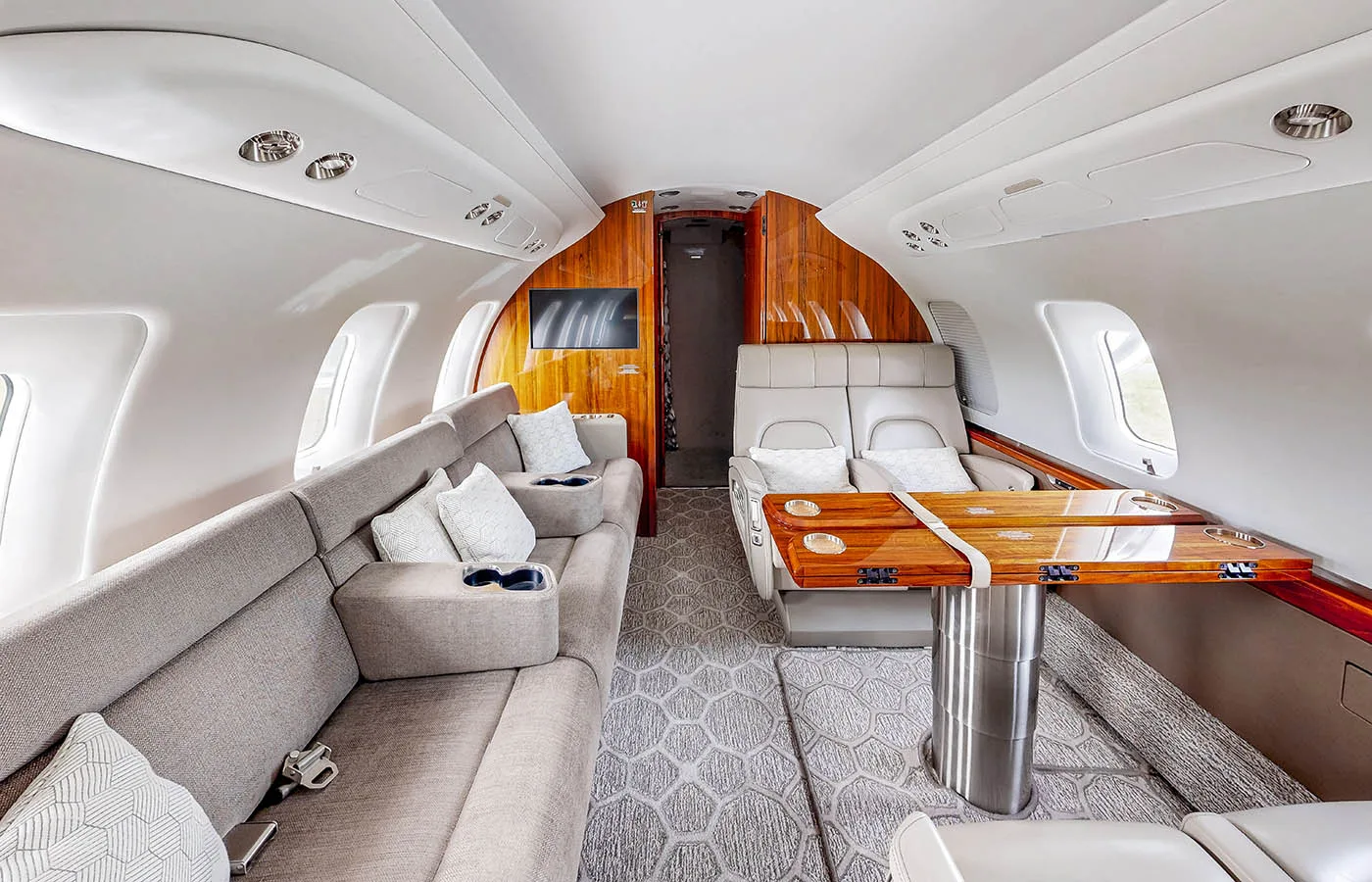 The luxurious cabin interior of a private jet features a grey sofa, a wooden table, and individual seats.