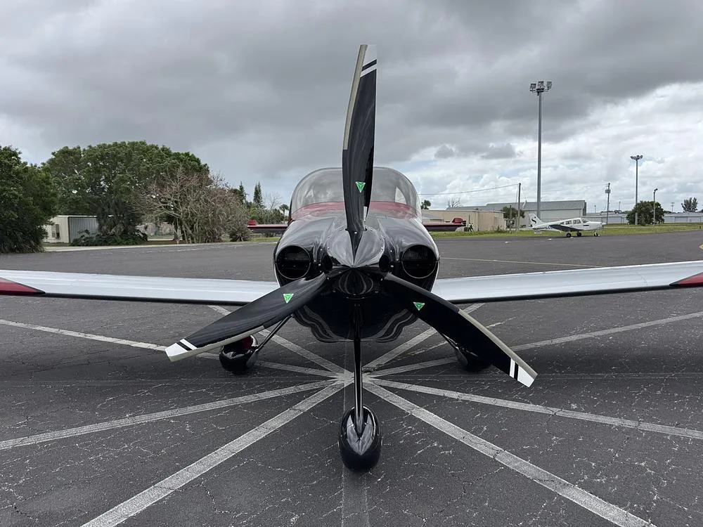Head-on view of a red, silver, and black single-engine aircraft (N113KC) with its propeller centered on an airport tarmac.