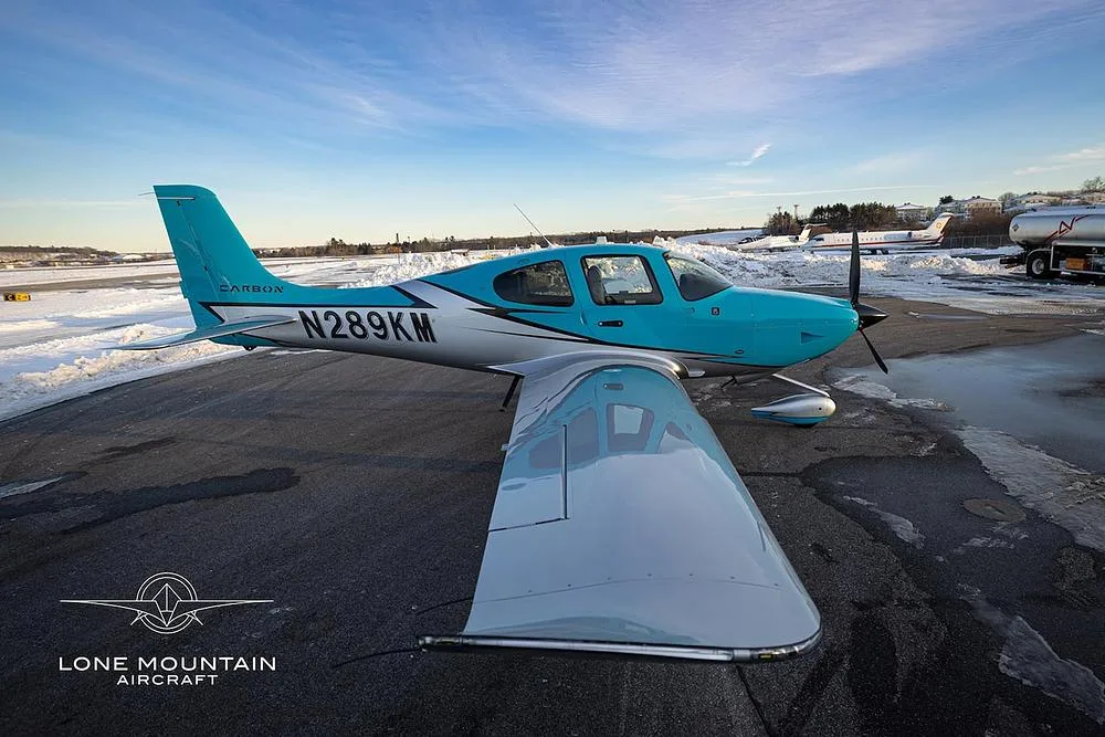 A three-quarter front view of a turquoise and silver single-engine aircraft, N289KM, parked on a snowy airfield.