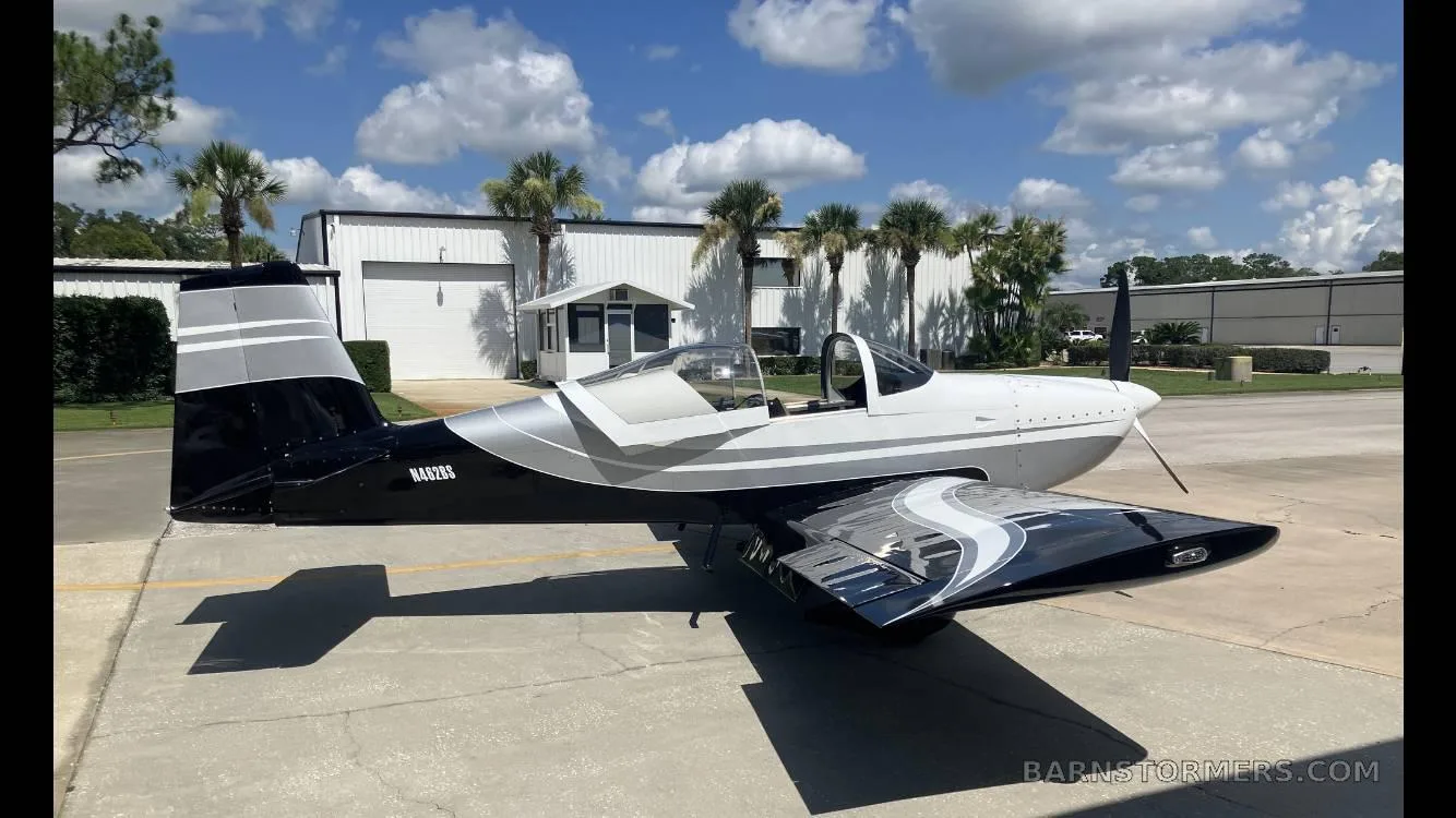 A white and black single-engine aircraft with silver accents and tail number N4929S is parked on a tarmac under a blue sky.