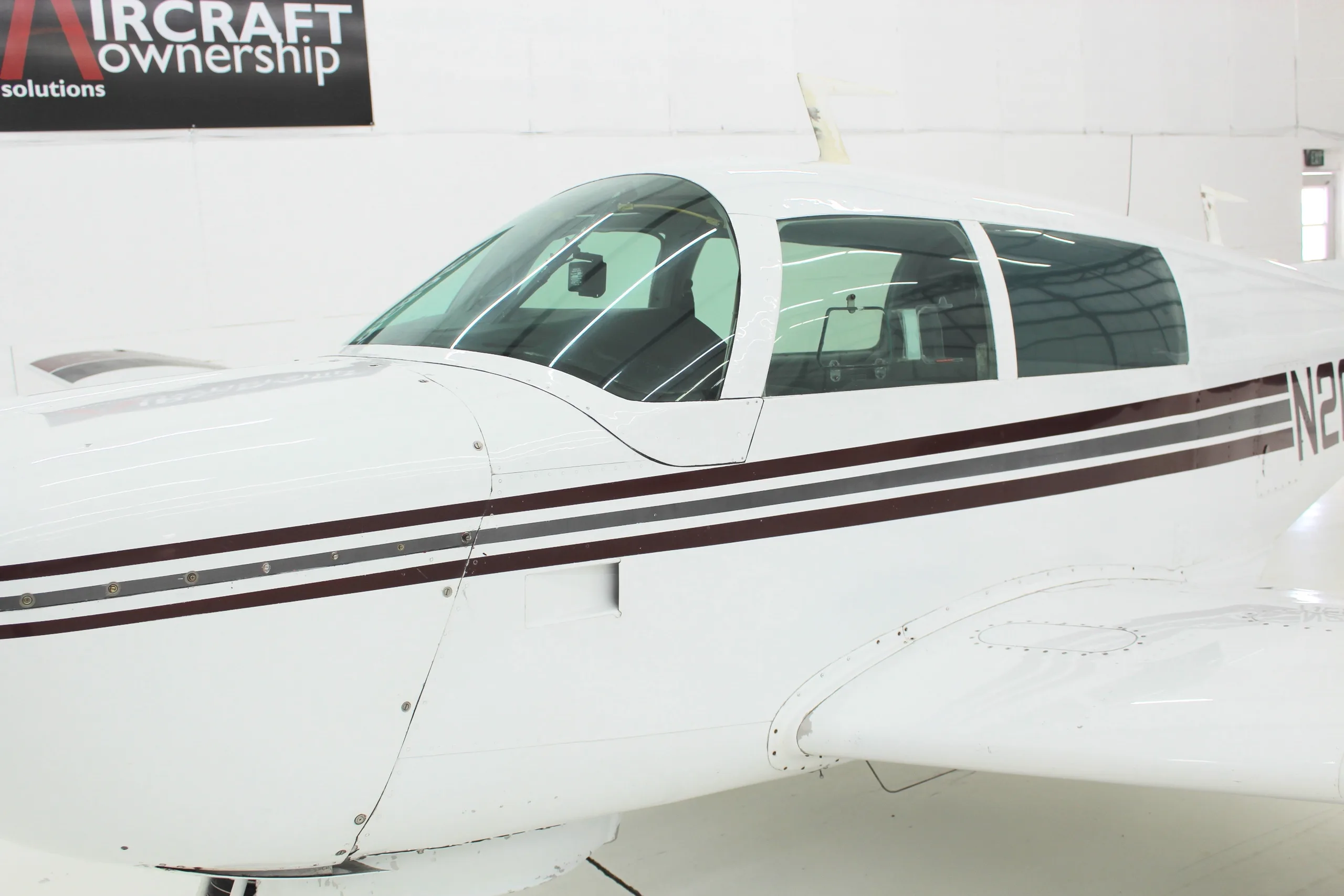 Close up of the cockpit and wing of the white and brown N201BP aircraft in a hangar.