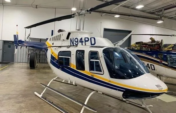 A white and blue helicopter with yellow stripes, N94PD, viewed from the front-right in a hangar.