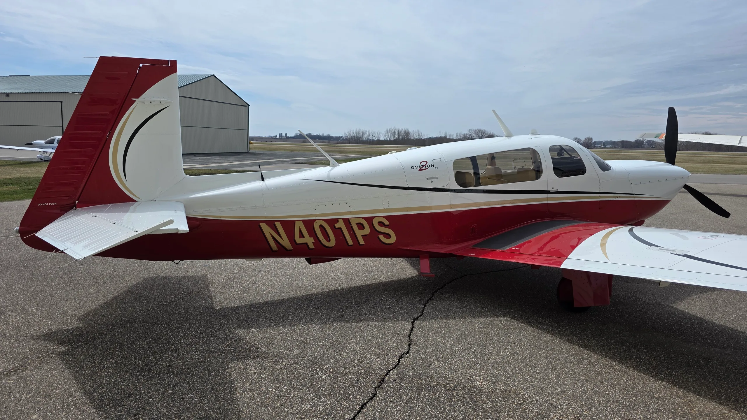 A red and white Mooney aircraft with registration N401PS parked on an asphalt apron, viewed from the rear right.