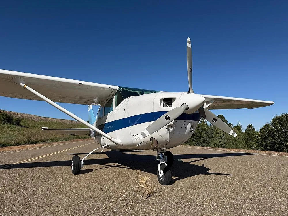 A head-on view of the white and blue single-engine aircraft N3746, highlighting its propeller, nose, and front landing gear on an asphalt strip.