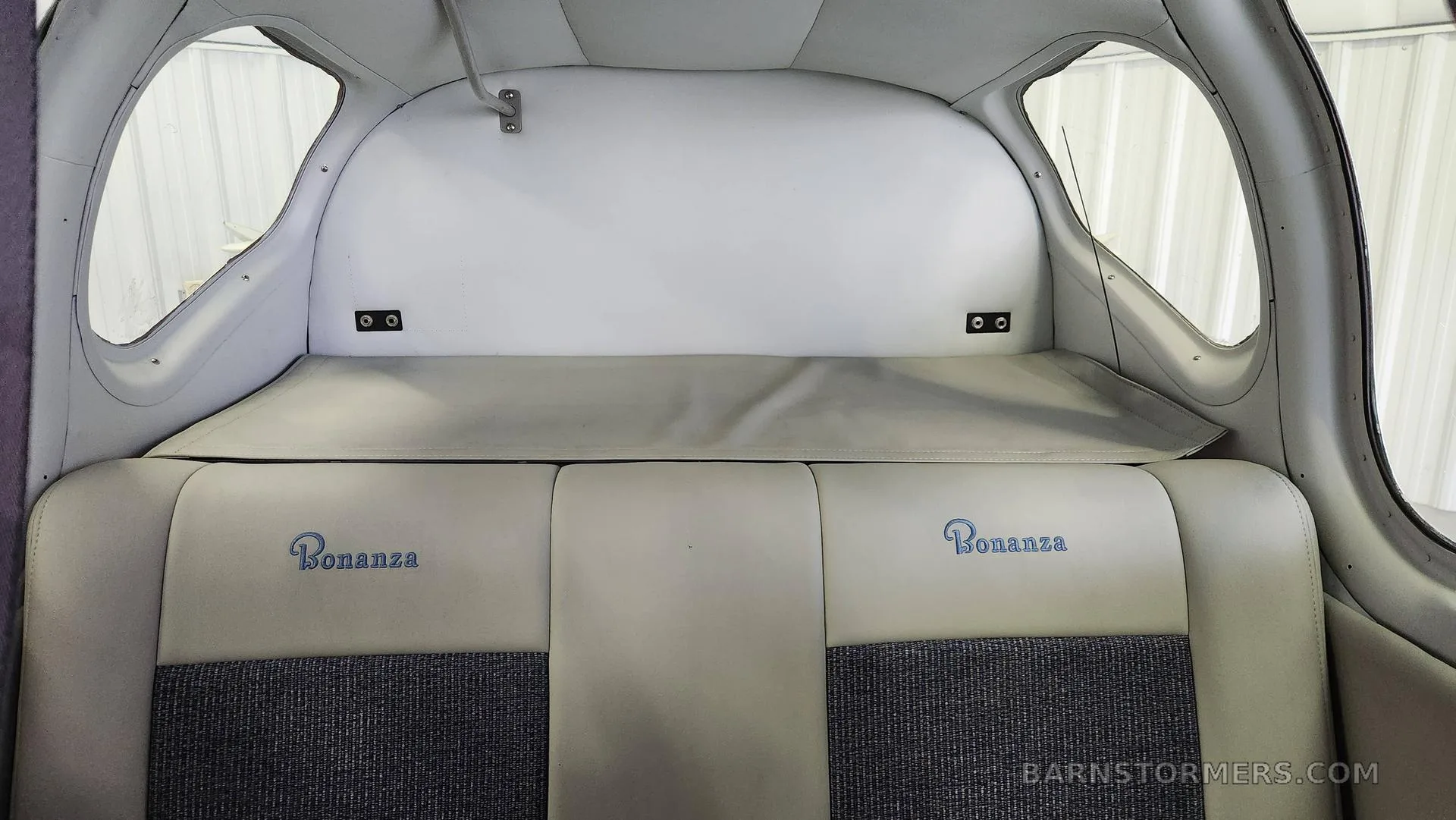 The rear cabin interior of an aircraft, showing two light-colored seats with "Bonanza" embroidered on them and a cargo shelf behind.