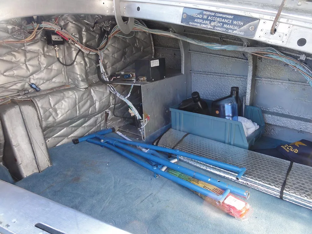 The aircraft's baggage compartment showing exposed wiring, insulation, and some stored items like a blue folding frame.