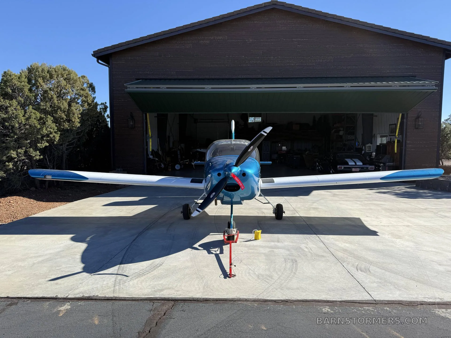 A blue and white RV-12 SLSA aircraft (N122PF) is parked head-on outside a hangar with its propeller pointed forward.