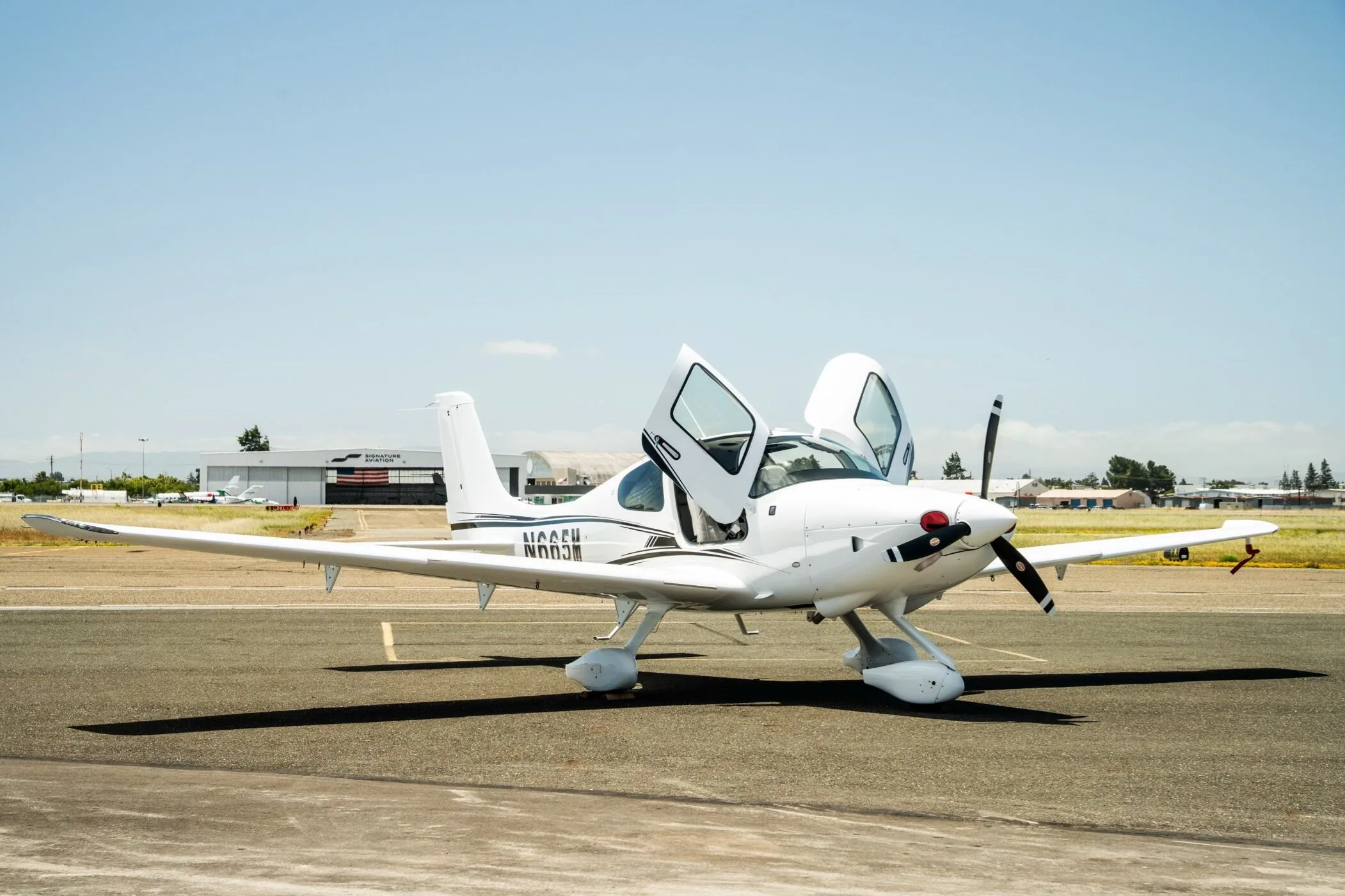 A white Cirrus SR22 aircraft with registration N665M parked on the tarmac with both doors open, viewed from the front.